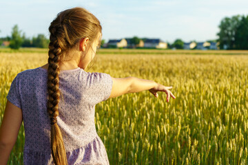 Back view of a beautiful little girl in a yellow wheat field during a sunset walk