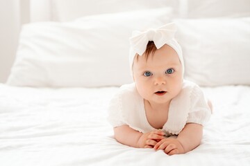 happy smiling newborn baby girl in white clothes on the bed at home, cute baby crawling, space for...