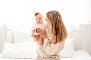 a mother with a newborn baby in her arms at home on a white background of a bed or window, a space...