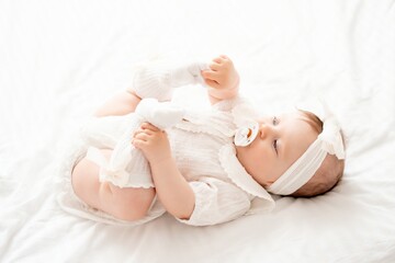 Cute newborn baby girl sucks a pacifier in white clothes on the bed at home on her back, cute baby...