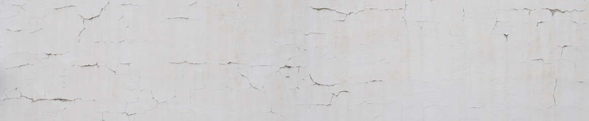 White facade with cracks and damage on the surface. Paint peeling off due to weather conditions. Monochrome architecture background in wide panoramic landscape format. Vintage surface.