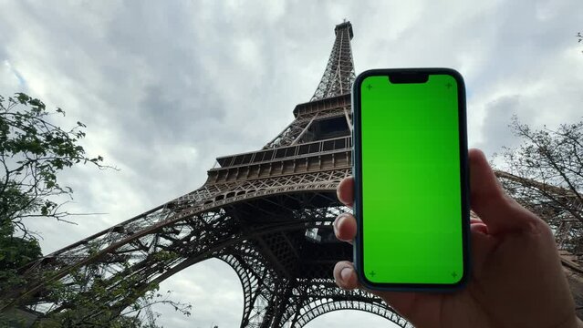 Man holds smartphone outside Eiffel Tower in Paris. Green screen mock up.