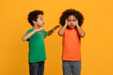 Two African American boys, engaged in a heated argument, are pictured against a bright yellow...