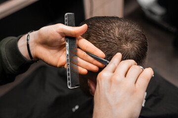 Barber styles the mans hair with scissors and comb at the barbershop. 