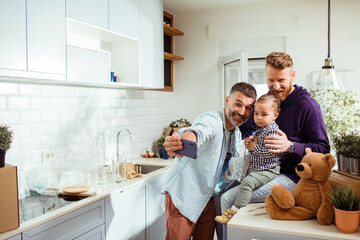 Two dads and toddler son taking a selfie in kitchen