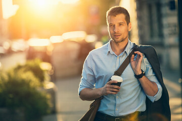 Businessman walking in city with coffee during sunset