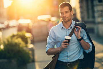 Businessman walking in city with coffee during sunset