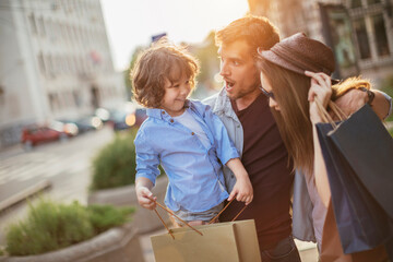 Young family with child on city street holding shopping bags