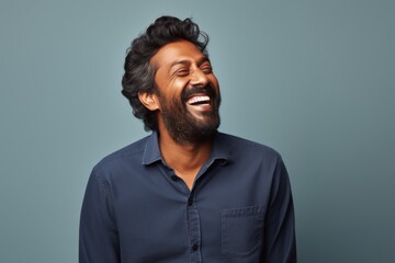 Fototapeta premium Portrait of a grinning indian man in his 30s laughing in front of blank studio backdrop