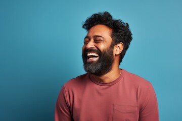 Obraz premium Portrait of a grinning indian man in his 30s laughing while standing against blank studio backdrop