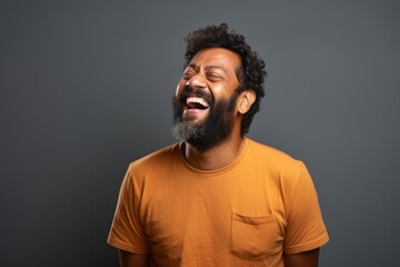 Fototapeta premium Portrait of a grinning indian man in his 30s laughing over blank studio backdrop