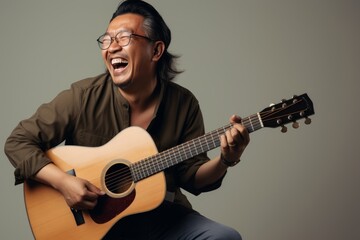 Obraz premium Portrait of a cheerful asian man in his 30s playing the guitar isolated in blank studio backdrop