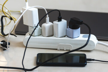 Electrical outlet with many chargers connected to it for a smartphone, laptop, microphone