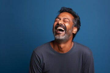 Portrait of a tender indian man in his 40s laughing on blank studio backdrop