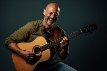 Portrait of a grinning man in his 40s playing the guitar over blank studio backdrop