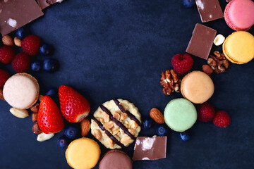 Macarons, chocolate, cookies, berries and various nuts on dark blue background. Top view.