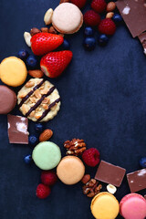 Macarons, chocolate, cookies, berries and various nuts on dark blue background. Top view.