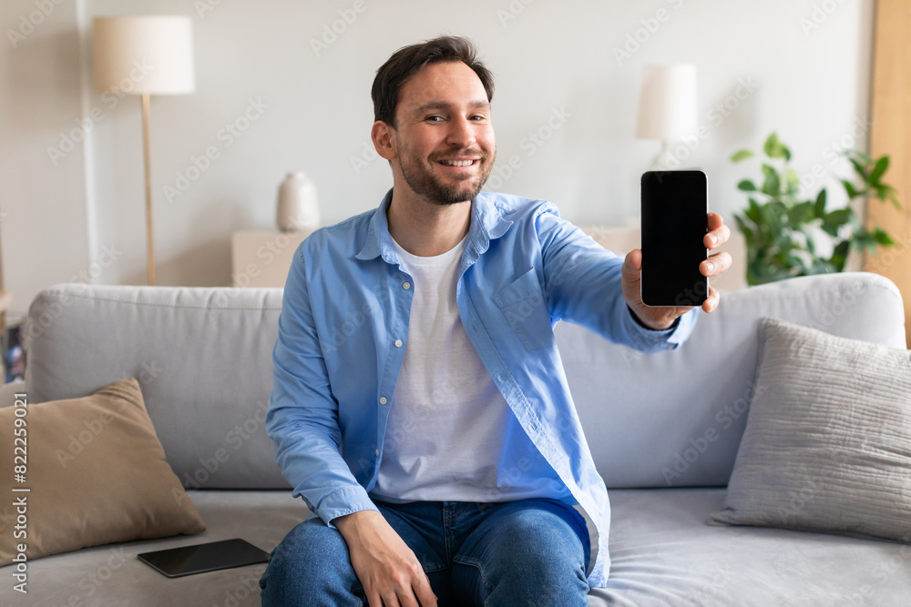Poster a man is seated on a couch, holding a smartphone in his hand. he appears focused on the screen, poss