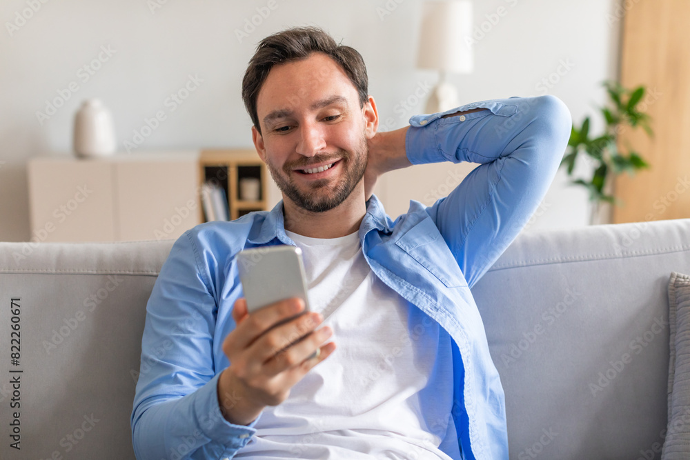Poster a man is sitting on a couch, engaged with his smartphone. he is focused on the devices screen, appea