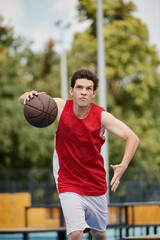 Fototapeta premium A young man confidently holds a basketball on top of a vibrant basketball court under the bright sun of a summer day.