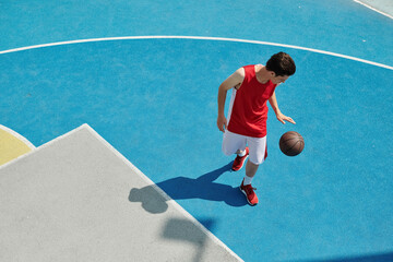 A young man stands on a basketball court holding a ball, preparing to play on a sunny day.
