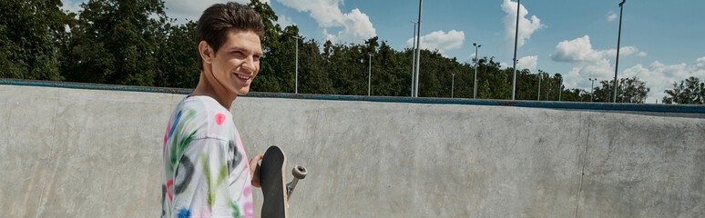 A youthful man adorned in a vibrant shirt joyfully holds a skateboard in a bustling skate park on a...