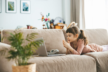 Resting on a comfortable sofa, a young girl, watching a laptop, her attention fixed on the screen....