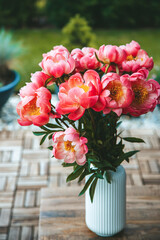 A beautiful bouquet of vibrant pink peonies with lush petals. Flowers are housed in a white vase with vertical ridging