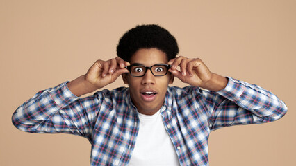 Surprised african-american student touching glasses feeling shocked, white background
