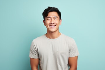 Obraz premium Portrait of a cheerful asian man in his 20s smiling at the camera in front of blank studio backdrop