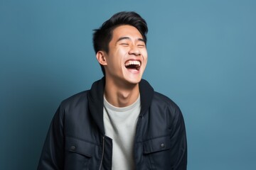 Portrait of a joyful asian man in his 20s laughing isolated in blank studio backdrop