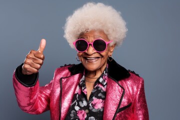Portrait of a merry afro-american elderly woman in her 90s showing a thumb up isolated on blank studio backdrop