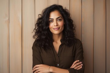 Portrait of a blissful indian woman in her 30s with arms crossed in front of light wood minimalistic setup