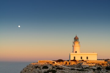 vertical view of the Cap de Cavalleria Lighthouse on Menorca at sunset with a full moon rising