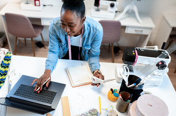 Female fashion tailor working on dress design in her workshop using laptop.