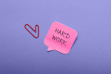 A red clip is on a pink piece of paper that says hard work.