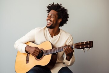 Portrait of a smiling afro-american man in his 20s playing the guitar on light wood minimalistic...