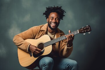 Portrait of a smiling afro-american man in his 20s playing the guitar in front of light wood minimalistic setup