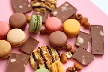 Pastel macarons, almond chocolate, peanut butter cookies and various nuts on bright pink background. Selective focus.