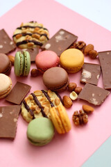 Pastel macarons, almond chocolate, peanut butter cookies and various nuts on bright pink background. Selective focus.