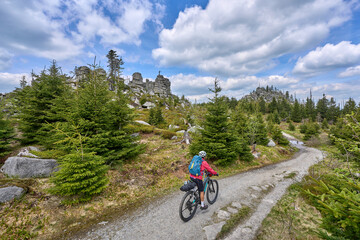 Naklejka premium active senior woman on a bike packing tour with her electric mountain bike in the rocky the summit of Great Arber in the Bavarian Forest, Bavaria, Germany