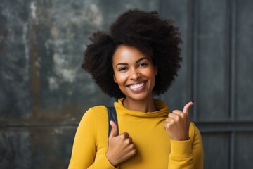 Fototapeta premium Portrait of a blissful afro-american woman in her 40s showing a thumb up in front of empty modern loft background