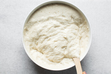 Overhead view of nigerian puff-puff dough that has proofed, puff-puff dough in a white mixing bowl,...