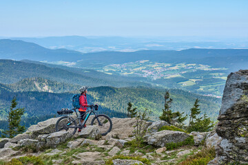 active senior woman on a bike packing tour with her electric mountain bike in the rocky  the summit of Great Arber in the Bavarian Forest, Bavaria, Germany