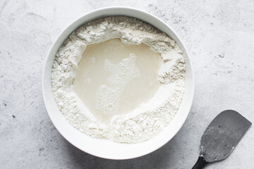 Overhead view of nigerian puff-puff dough being mixed with a wooden spoon, puff-puff dough in a white mixing bowl, process of making puff-puff or bofrot