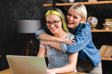 Homosexual couple girlfriends lgbtq lesbians sisters co-workers working together, studying, doing project, collective team work while hugging cuddling bonding in home office