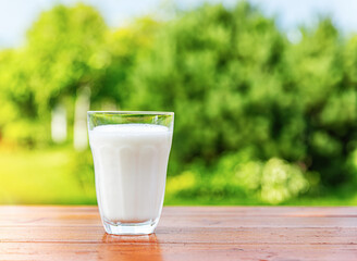 A glass of milk on a wooden table against the backdrop of a summer garden.