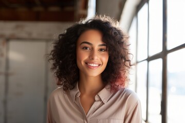 Portrait of a blissful indian woman in her 20s smiling at the camera while standing against empty modern loft background