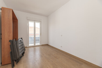A room with some furniture leaning against the wall and a balcony with glass doors in the background