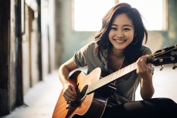 Portrait of a grinning asian woman in her 20s playing the guitar on empty modern loft background